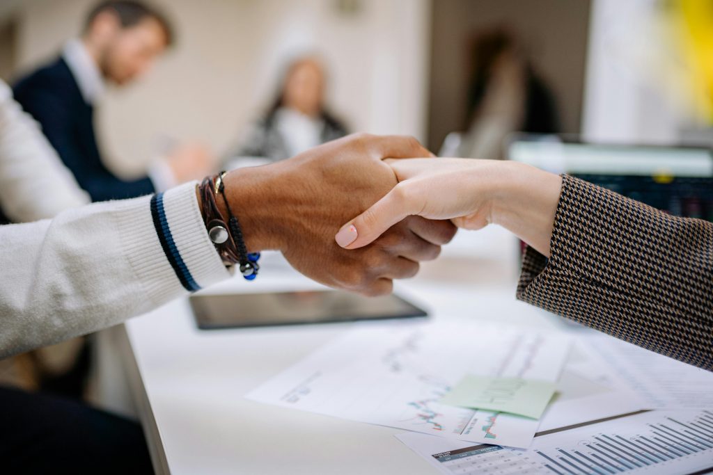 Two business professionals shaking hands across a desk during a meeting