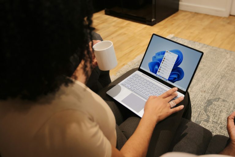 A person using a laptop at a desk with the Windows start screen displayed