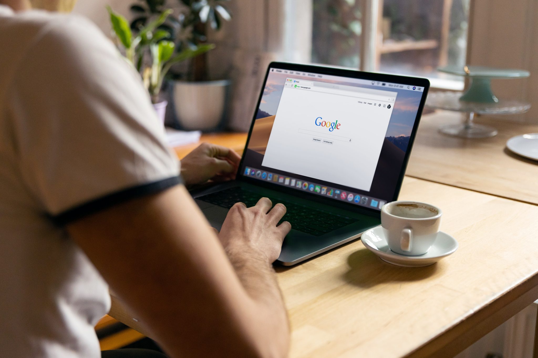 Person using a laptop open on the Google search page, with a cup of coffee on the desk